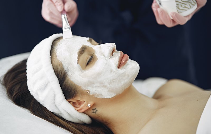A picture of a therapist putting a beauty treatment solution on the face of a client