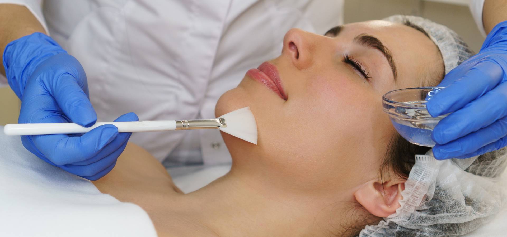 An image of a woman with her eyes closed, receiving a facial treatment.